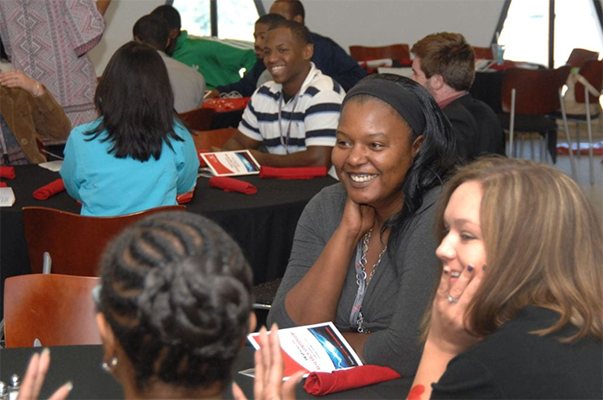 Groups of McNair Scholars smile and talk at round tables.