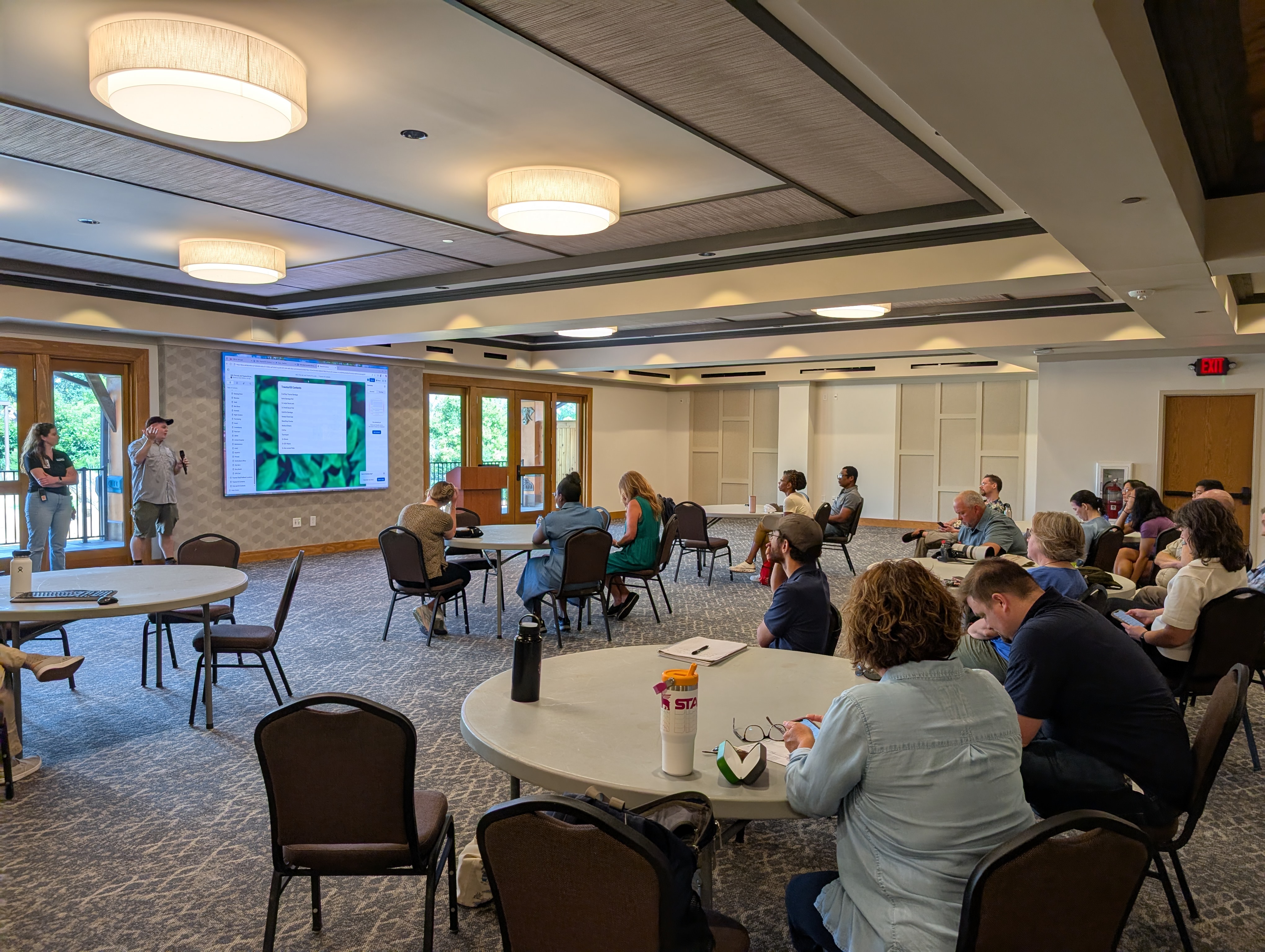 People sit at round tables in a conference room watching a presentation