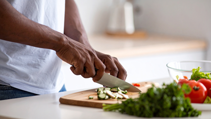 person's hands holding a knife chopping vegetables