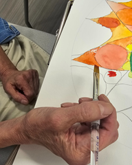 hand holding a paint brush in front of a painting during art therapy