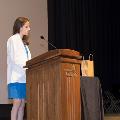 A woman in a white coat speaks at a podium